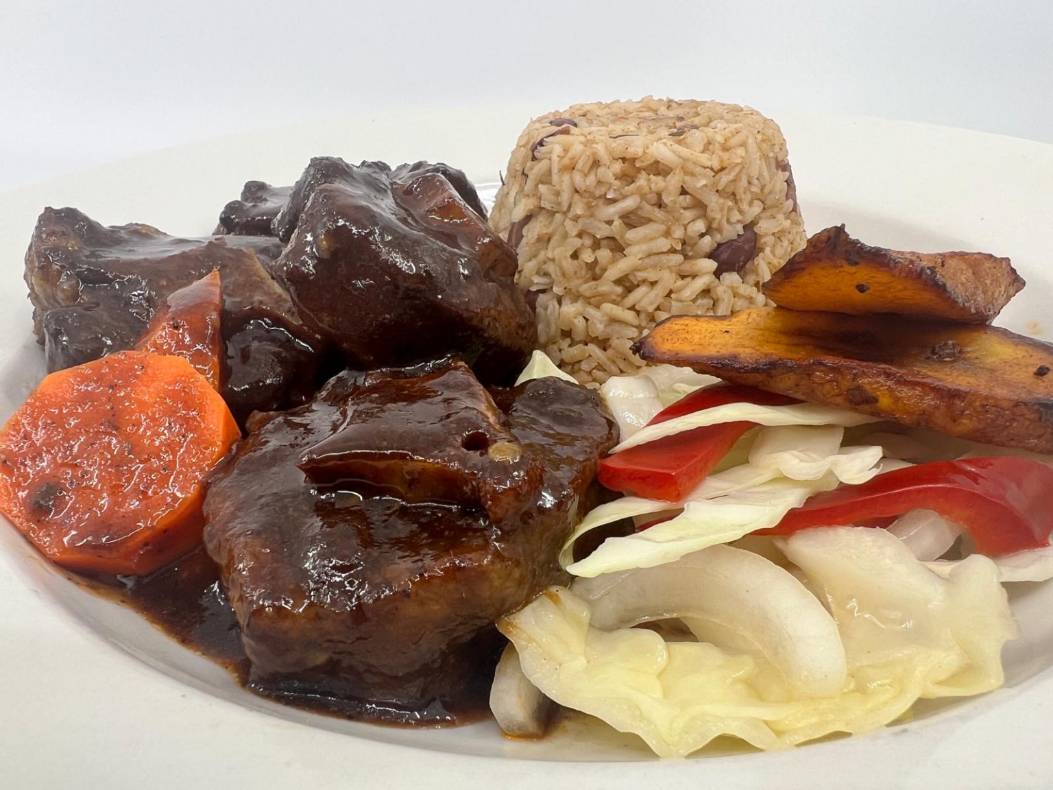 Jamaican oxtails served with rice and peas, plantains, and vegetables